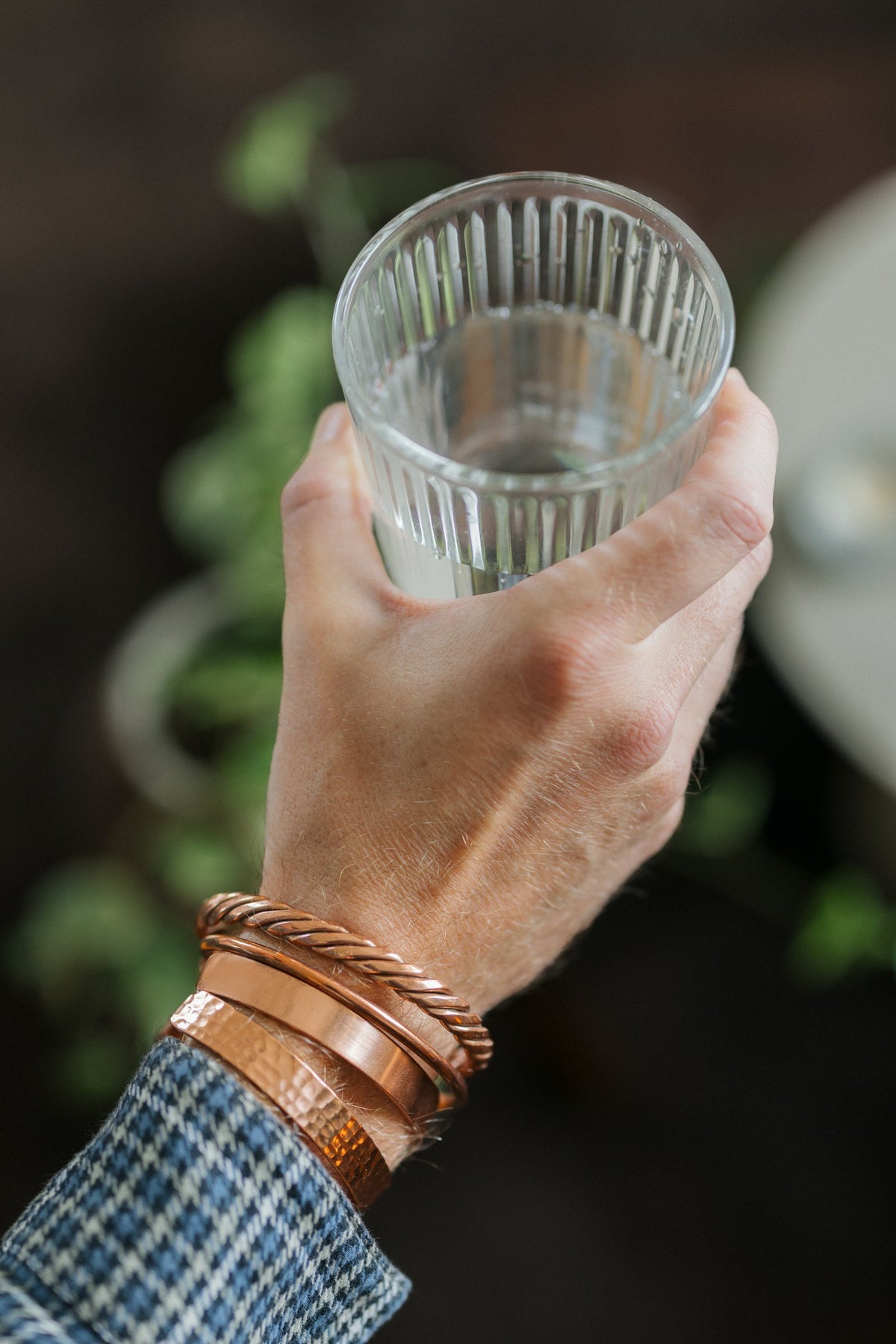 Kopero Koppararmband, alla fyra varianterna tillsammans runt en handled, med ett glas vatten i handen
