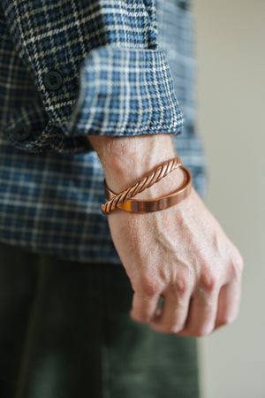 Kopero Koppararmband Tvinnat, på handleden över en rutig skjortärm, tillsammans med ett slätt armband