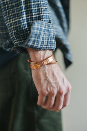 Kopero Koppararmband Hamrad, på handleden över en rutig skjortärm, tillsammans med ett slätt armband