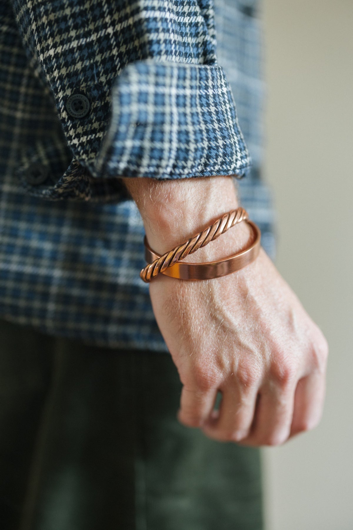 Kopero Koppararmband Slät, på handleden över en rutig skjortärm, tillsammans med ett tvinnat armband