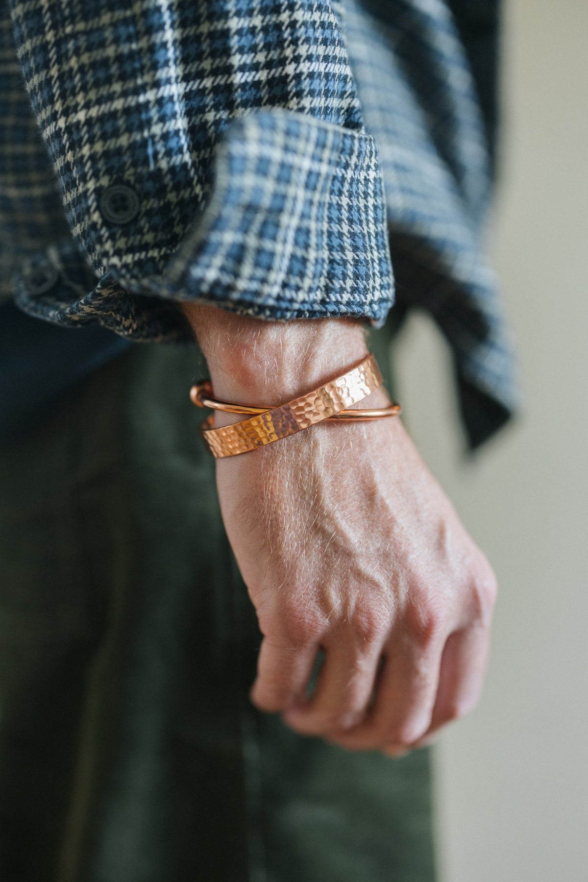 Kopero Koppararmband Runt, på handleden över en rutig skjortärm, tillsammans med ett hamrat armband