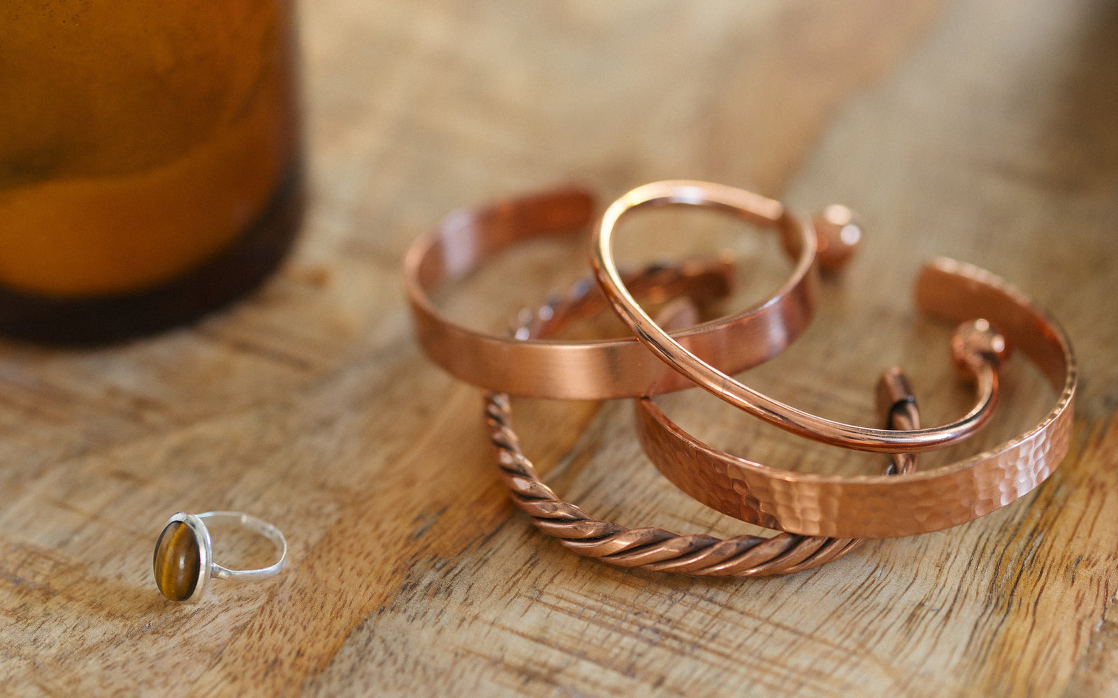 Fyra koppararmband, tvinnat, slätt, hamrat och runt, på ett träbord bredvid ett ljus och en ring