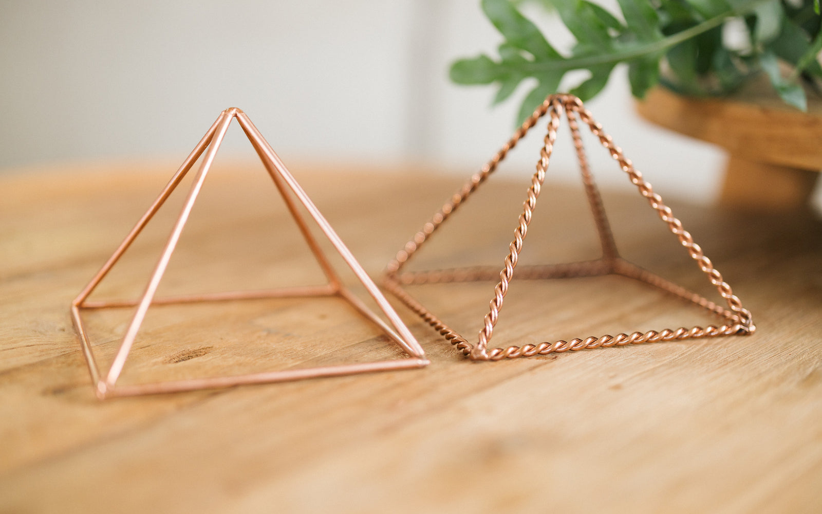 Två kopparpyramider, en tvinnad och en slät, bredvid varandra på ett träbord