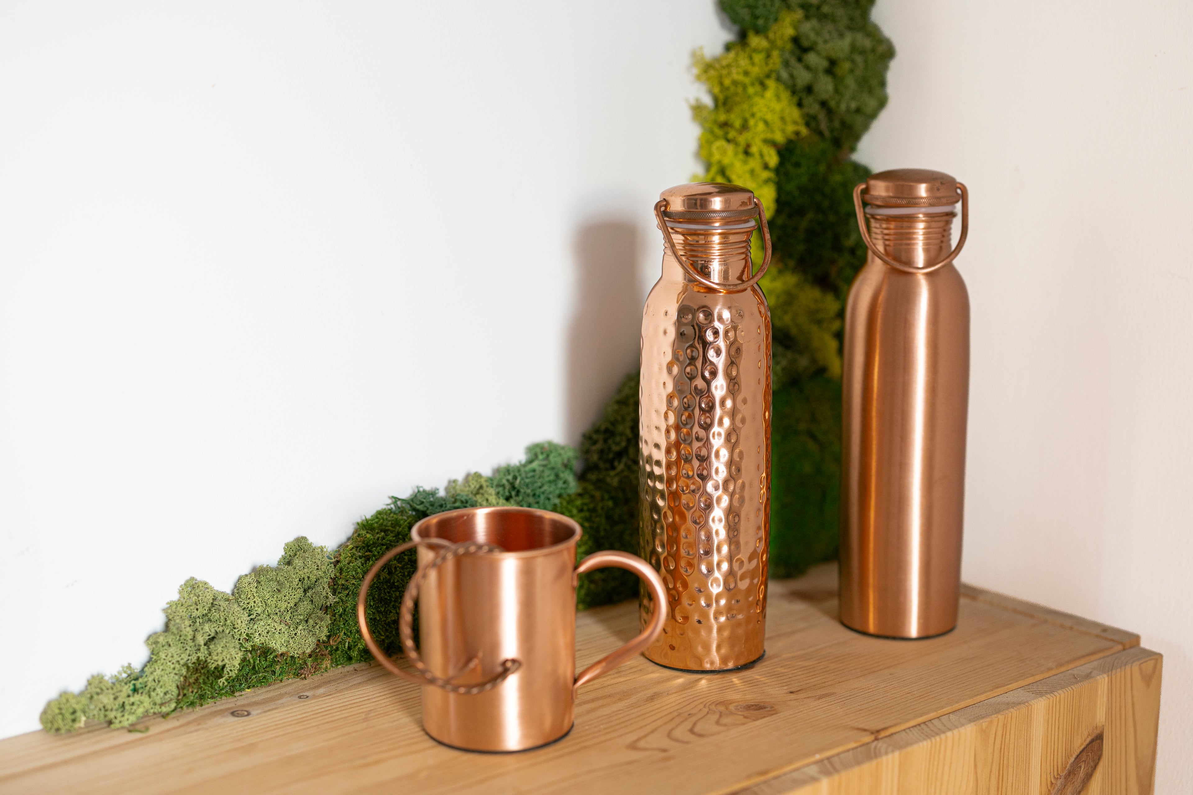 Kopero waterfles, mok en tensorring op een plank met mos, koperen woonaccessoires