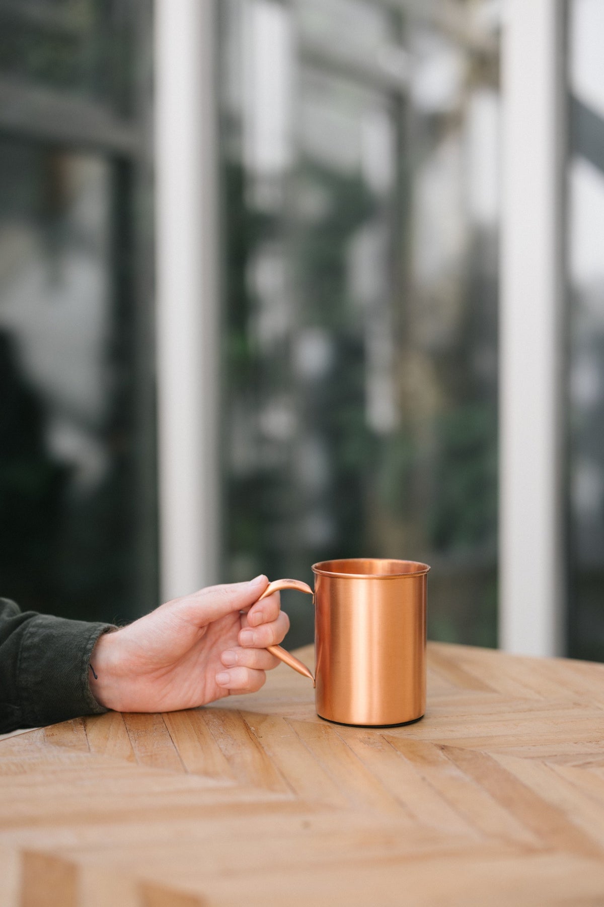Kopero Kopparmugg Slät, på ett träbord, med en hand på handtaget
