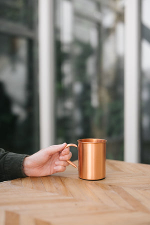 Kopero Kopparmugg Slät, på ett träbord, med en hand på handtaget