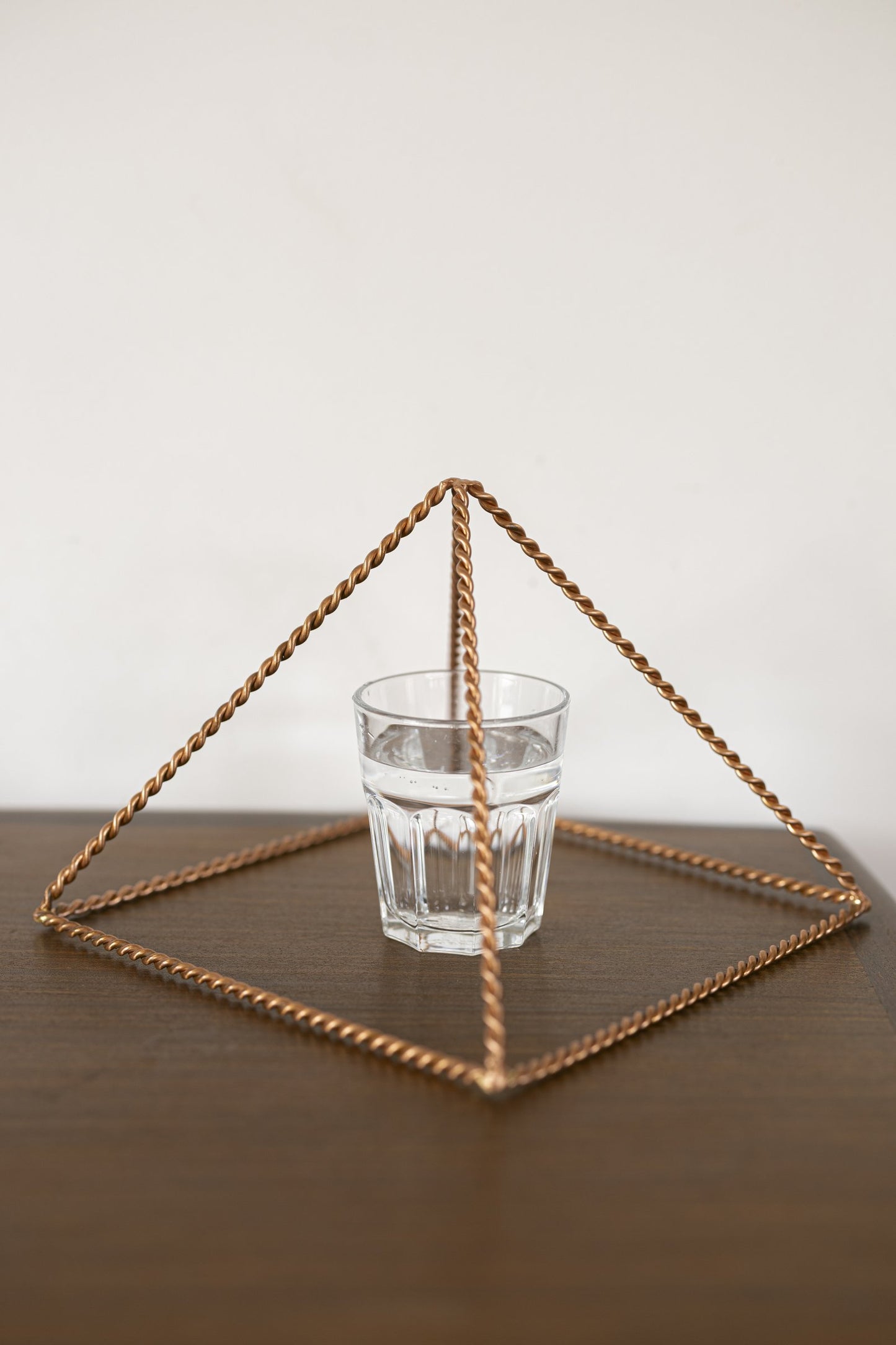 Kopero Kopparpyramid Energizer Tvinnad Stor (23,56 cm) ovanför ett glas vatten