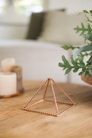 Kopero Kopparpyramid Energizer Tvinnad Liten (14,56 cm), på ett träbord bredvid ljus
