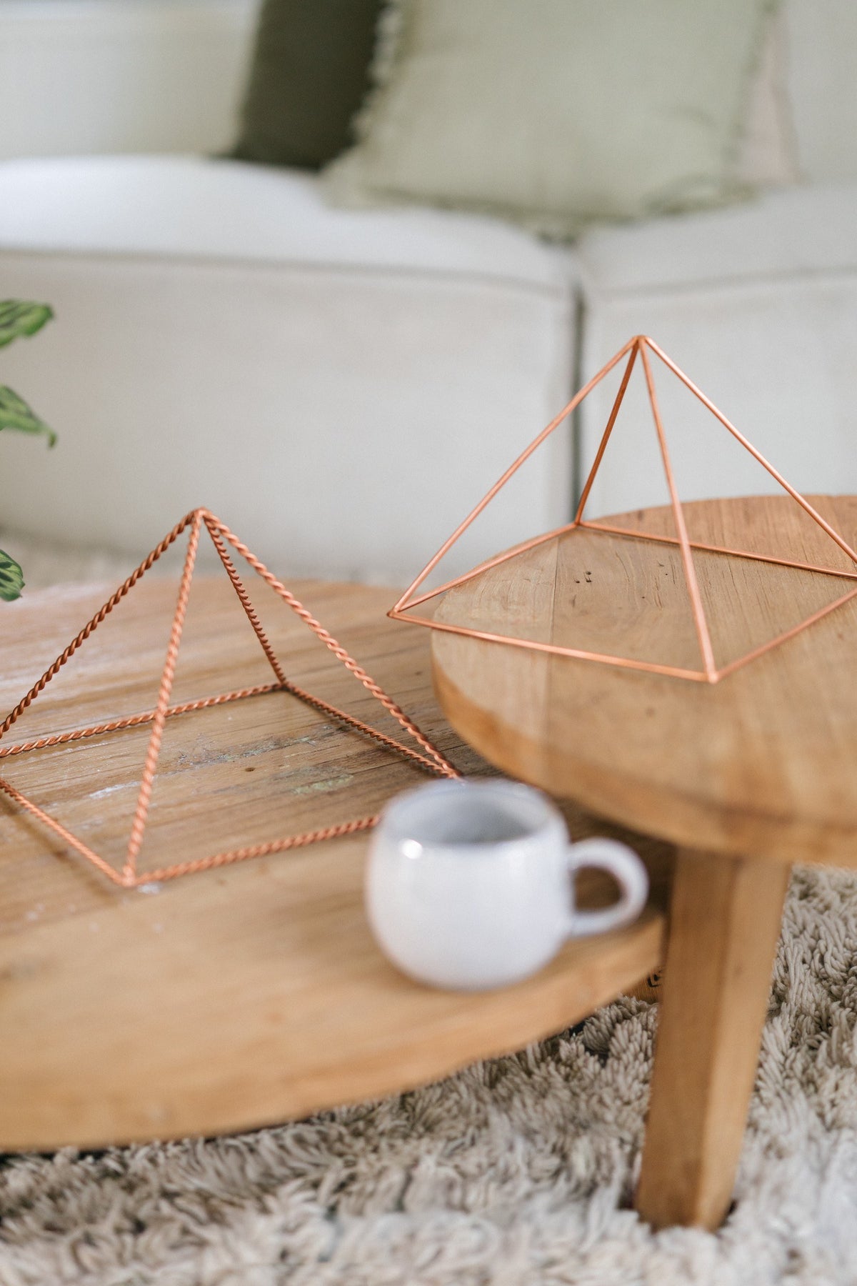 Kopero Kopparpyramid Energizer Slät Stor (23,56 cm), en tvinnad och en slät stor pyramid på två träbord med en mugg